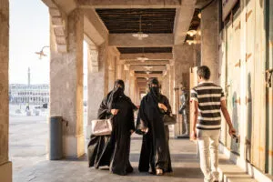 Două femei purtând hijab se plimbă pe unul dintre pasajele din souq, în timp ce un bărbat indian trece pe lângă ele și se uită la ele, Sursa foto dreamstime.com