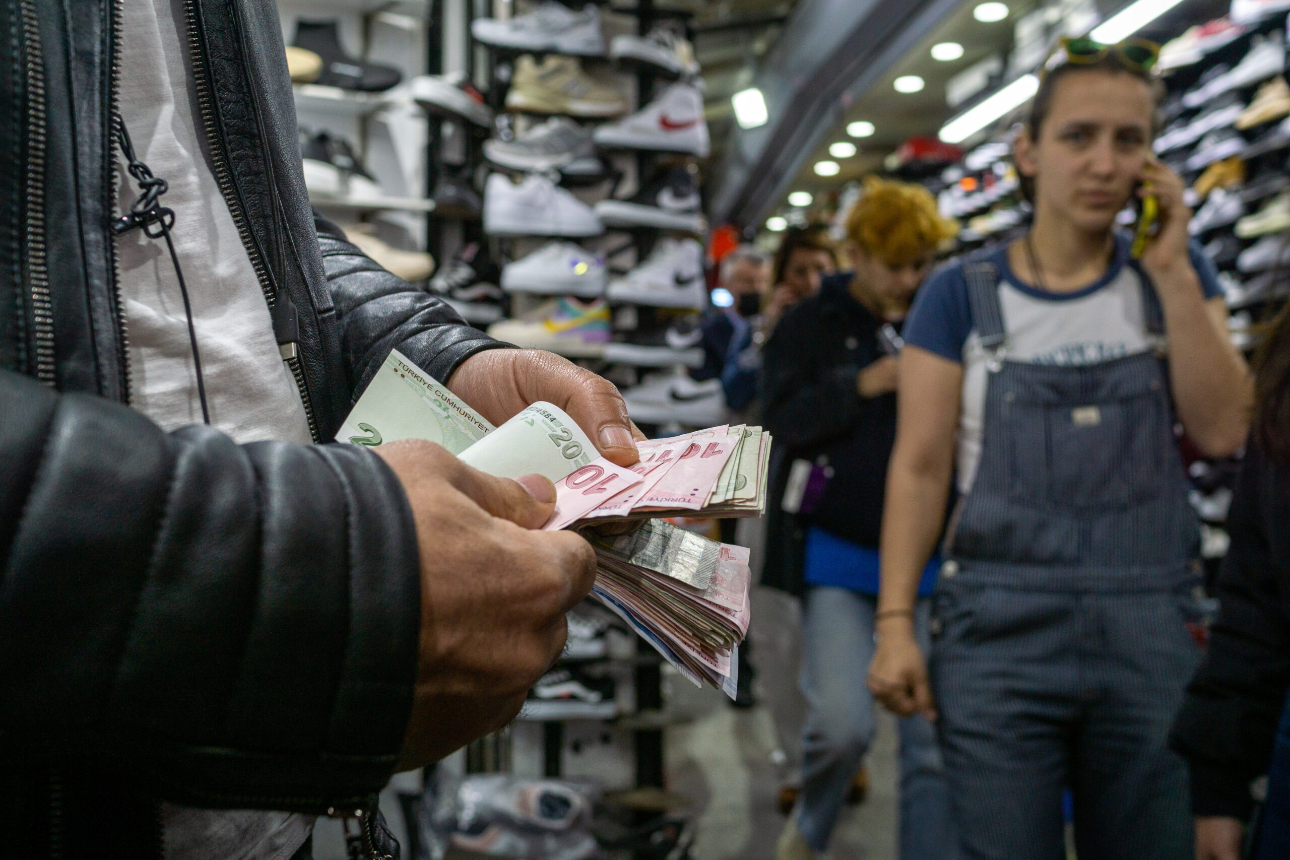 Bărbat numărând bani în piața de pantofi Kadikoy și clienți în fundal în faimosul cartier central al Istanbulului, Kadikoy Bazaar, pe 07 mai 2022, în Istanbul, Turcia. Inflația a urcat în aprilie în Turcia la aproape 70 69,97 pe un an, în aprilie, cel mai ridicat nivel din februarie 2002, potrivit cifrelor oficiale publicate pe 5 mai (dreamstime)