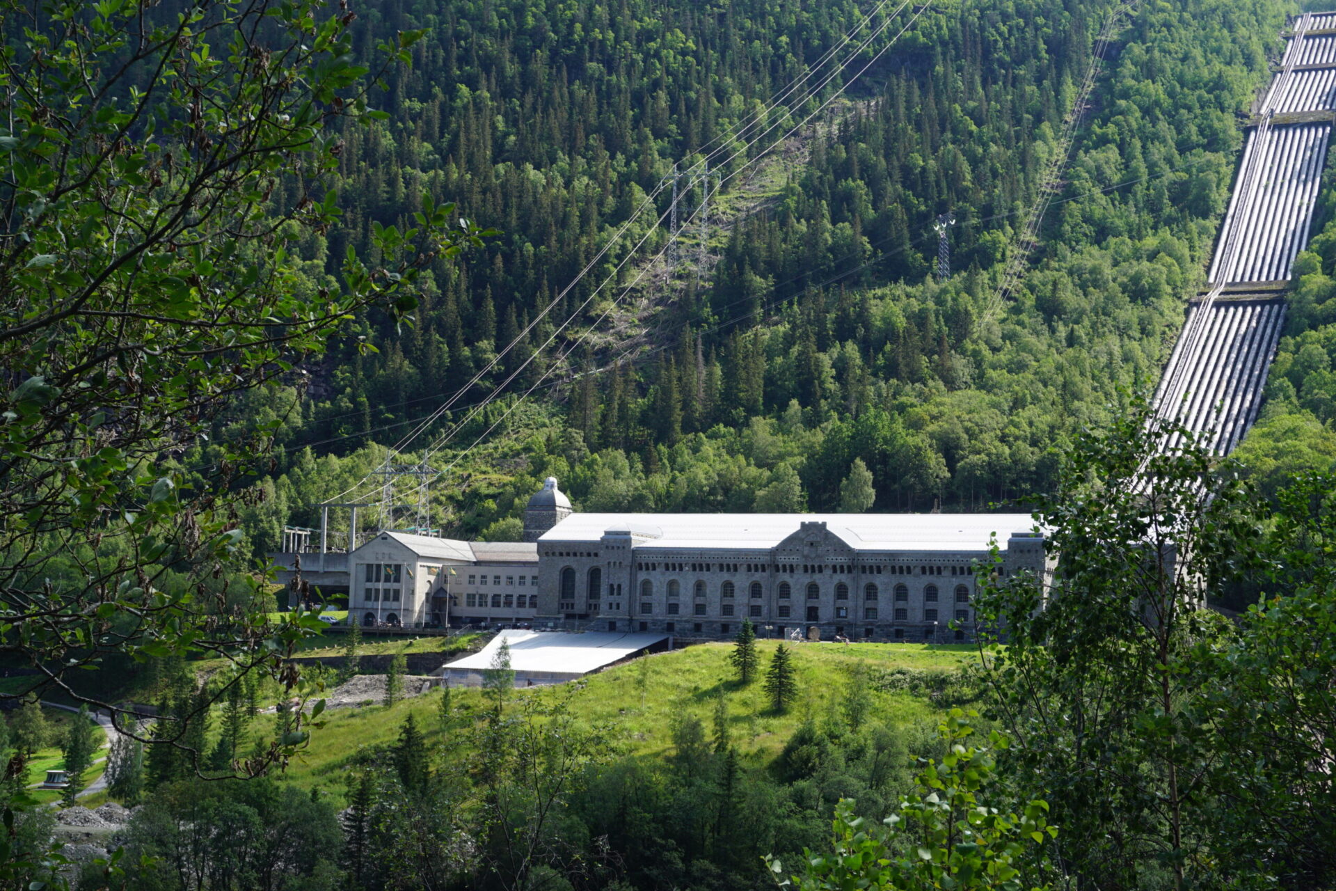 Hidrocentrala Vemork, clădirea veche a fabricii înconjurată de pădure verde cu conducte în fundal 