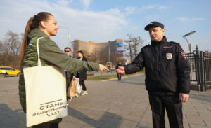 O tânără îi înmânează unui ofițer de poliție o broșură promoțională despre armată.