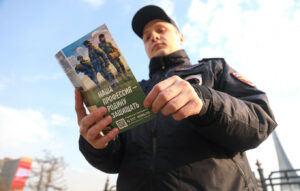 Un ofițer de poliție examinează o broșură promoțională pentru recrutare, pe a cărei copertă scrie: "Profesia noastră este de a apăra patria."
