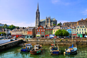 Clădiri colorate și bărci vechi cu catedrala în fundal în portul din Cobh, Cork, Irlanda, Sursa foto: dreamstime.com