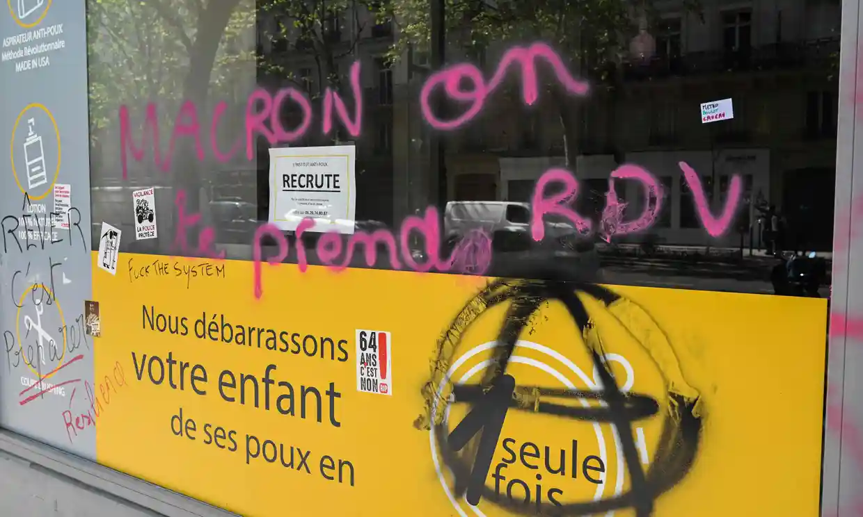 O fotografie ce arată o vitrină deteriorată ce afișează un graffiti pe care scrie „Macron, îți dăm întâlnire", pe 2 mai (sursă foto: The Guardian)